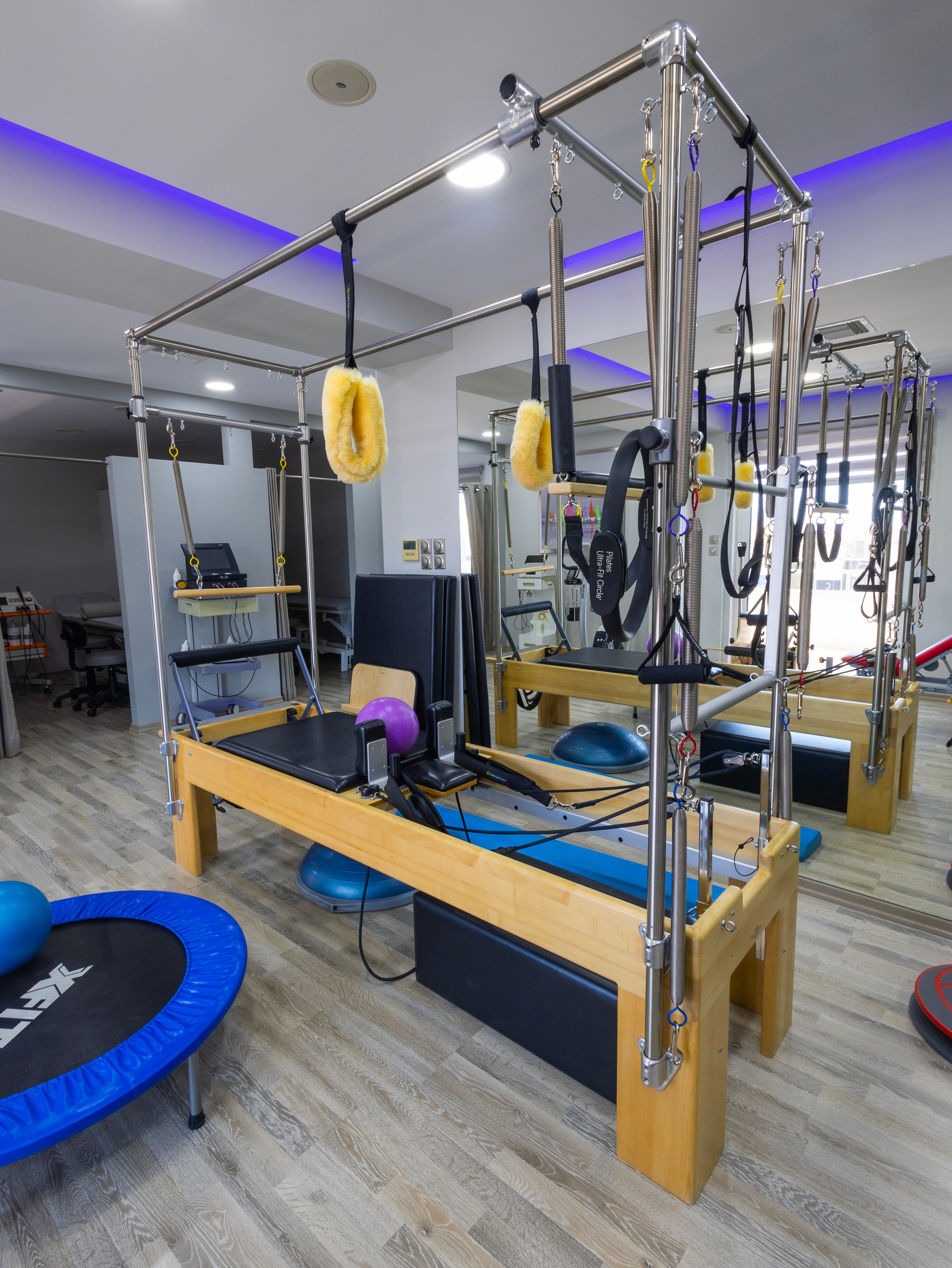 Συσκευή Pilates τύπου Cadillac με ιμάντες και εξαρτήματα, τοποθετημένη σε φωτεινό δωμάτιο με καθρέφτες.